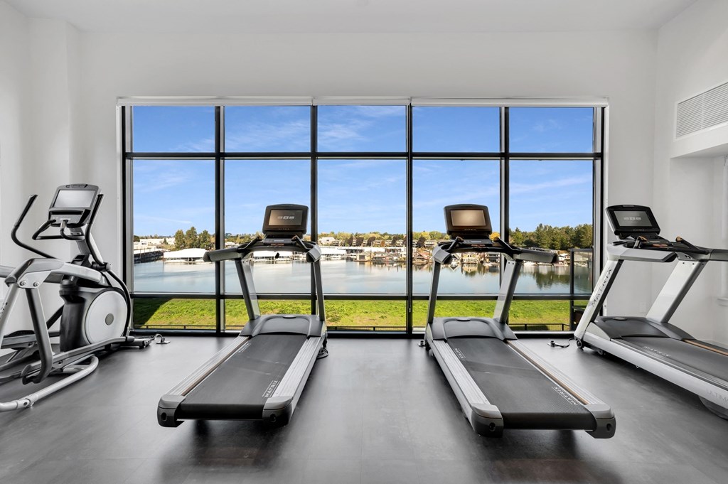 A gym with treadmills and elliptical machines with a view of the lake outside the window.