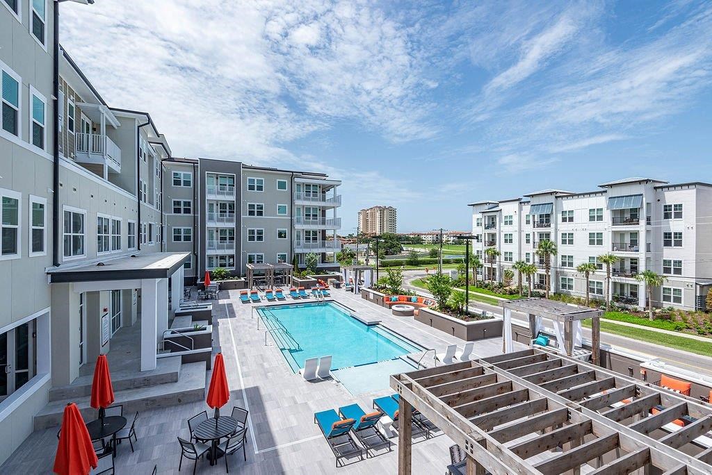 a swimming pool with lounge chairs and umbrellas in front of an apartment building