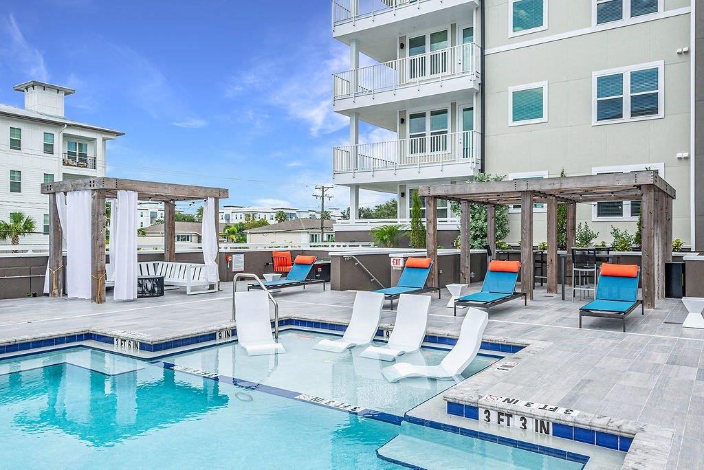 a swimming pool with chairs and a building in the background