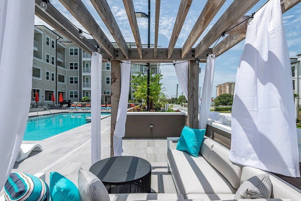 a pergola with blue and white pillows on a patio next to a pool