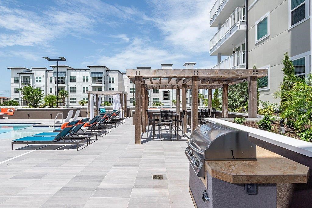 a patio with a grill and lounge chairs next to a swimming pool