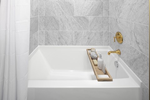 A white bathtub with a gold faucet and a tray with toiletries on it.