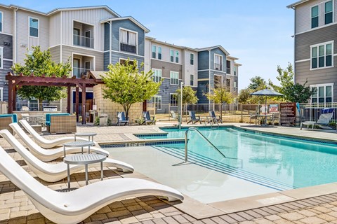 A pool area with sun loungers and a building in the background.