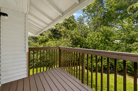 A wooden deck with a white house and trees in the background.