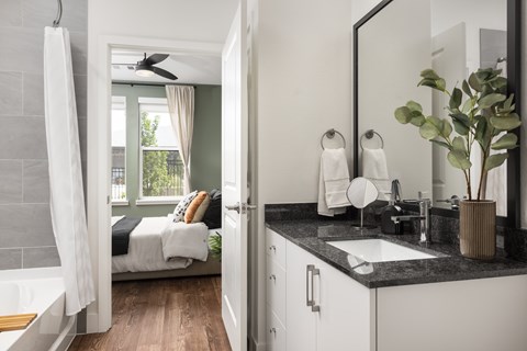 A bathroom with a large mirror and a bedroom with a window.