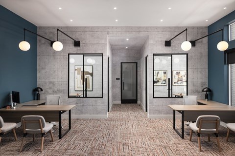 A modern office space with a carpeted floor, two desks with chairs, and a glass partition wall.