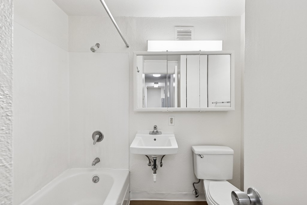 A white bathroom with a tub, sink, toilet and mirror.