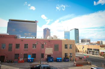 A city street with a blue car in the foreground and a large building with a flag on it in the background.