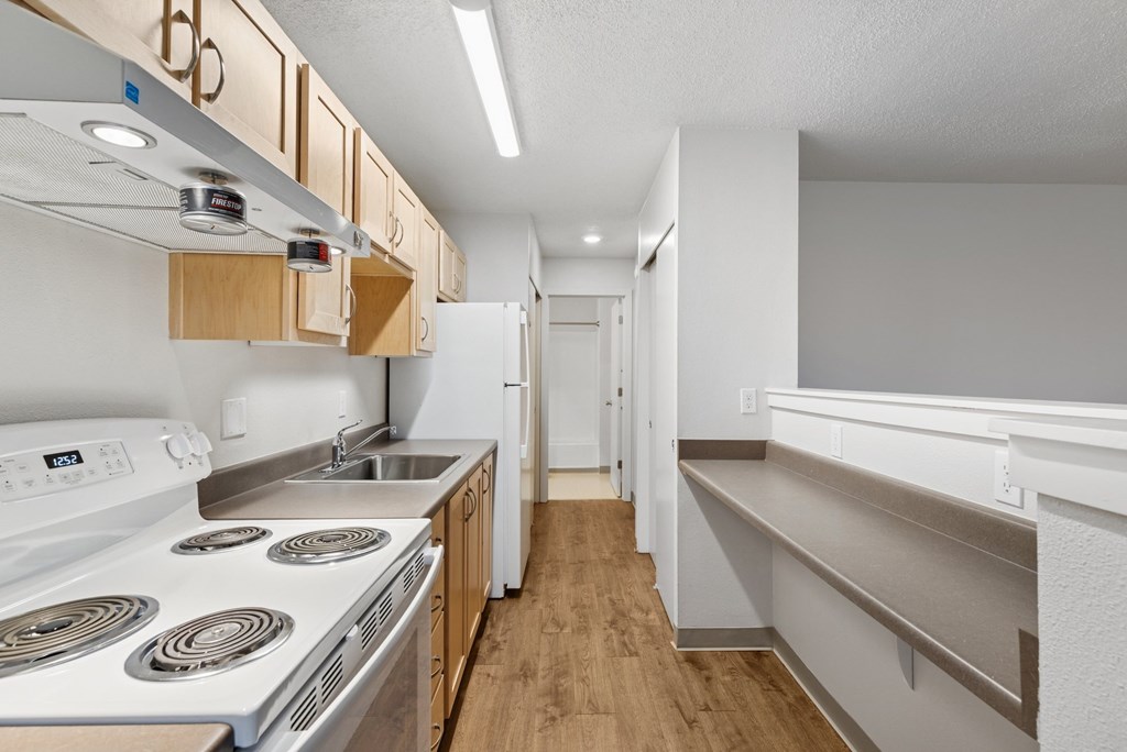 A kitchen with a white stove top oven and wooden cabinets.