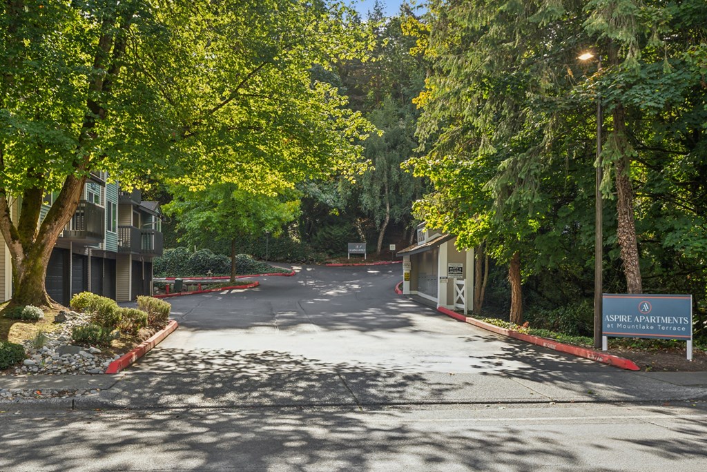 A tree-lined street with a sign for Aspire Apartments on the right.