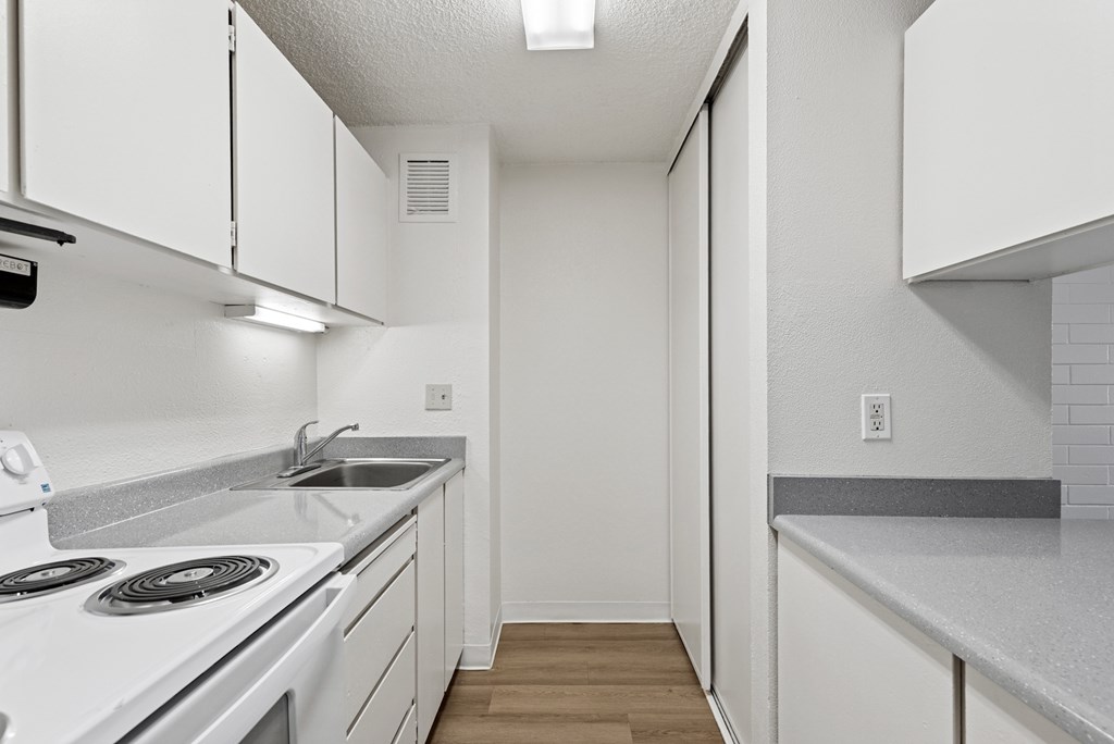 A white kitchen with a stove, sink, and cabinets.