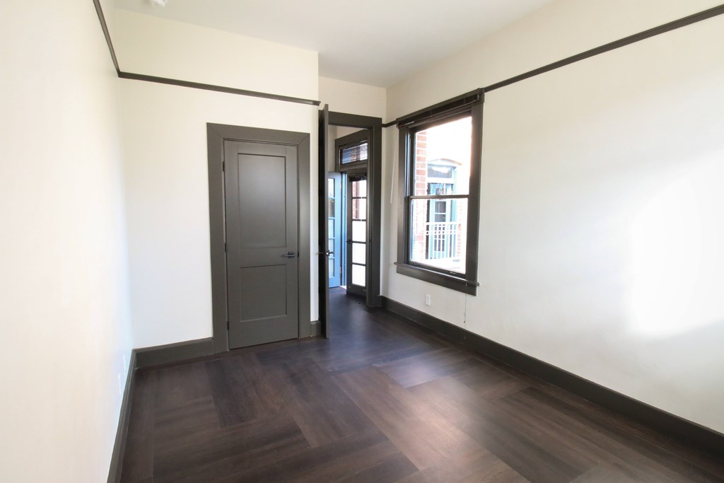 A room with a dark wood floor and a grey door.