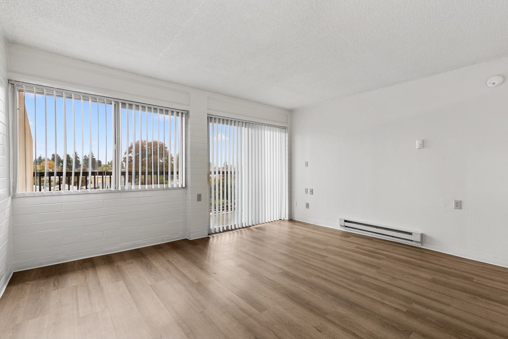 A room with wooden floors and white walls, with a window overlooking a tree-lined street.