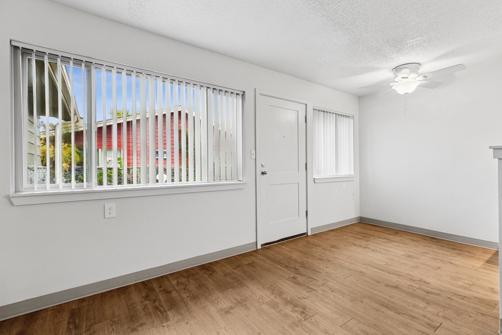A room with a window, wooden floor, and white walls.