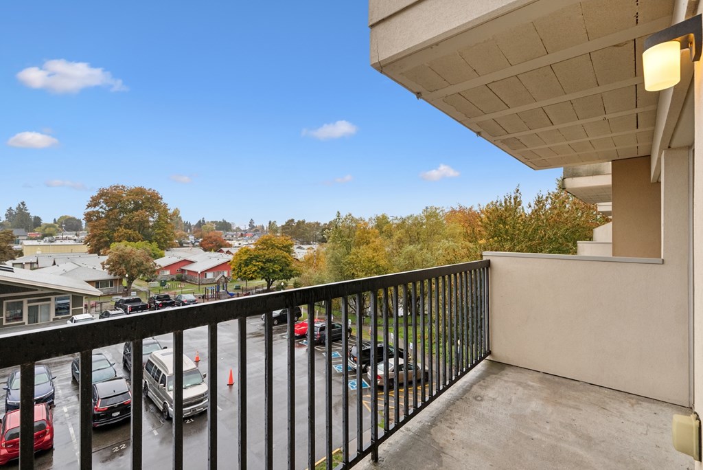 A balcony with a black railing overlooks a parking lot and trees.