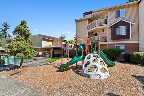 A playground with a slide and a climbing frame in front of a building.
