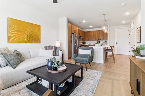 A modern living room with a white sofa, a grey armchair, a wooden dining table, and a yellow abstract painting on the wall.