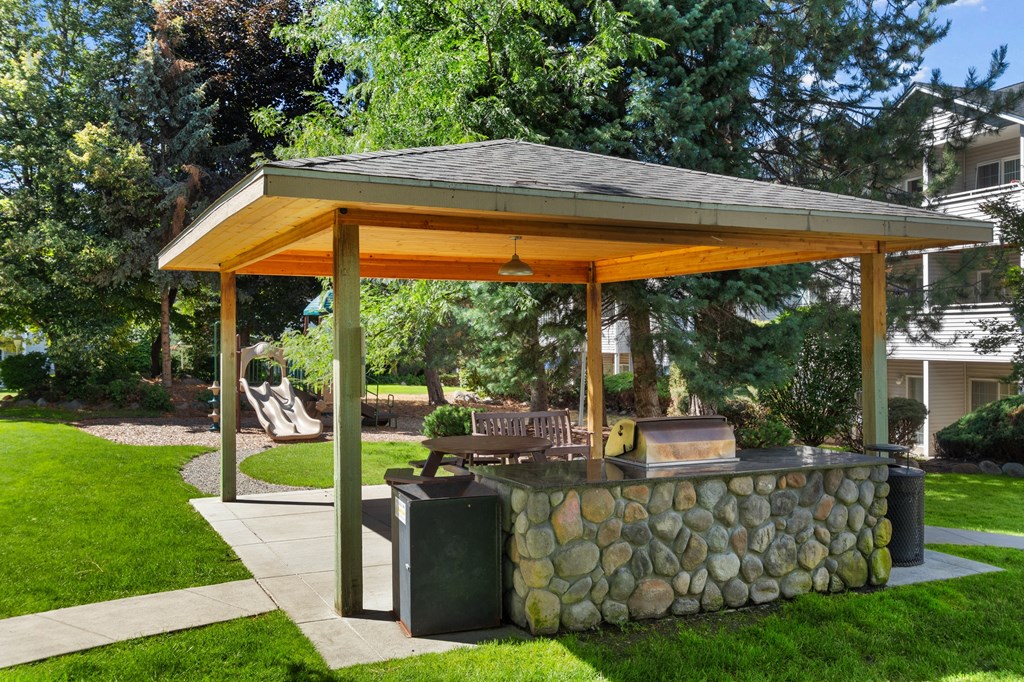 a stone patio with a pavilion with a grill