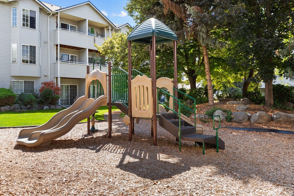 a playground with a slide and a swing set in front of an apartment building