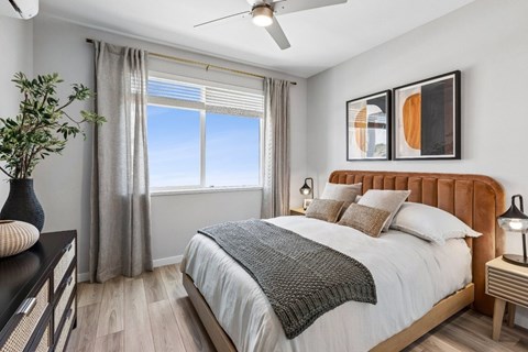 A bedroom with a large bed, a ceiling fan, and a window with a view of the sky.
