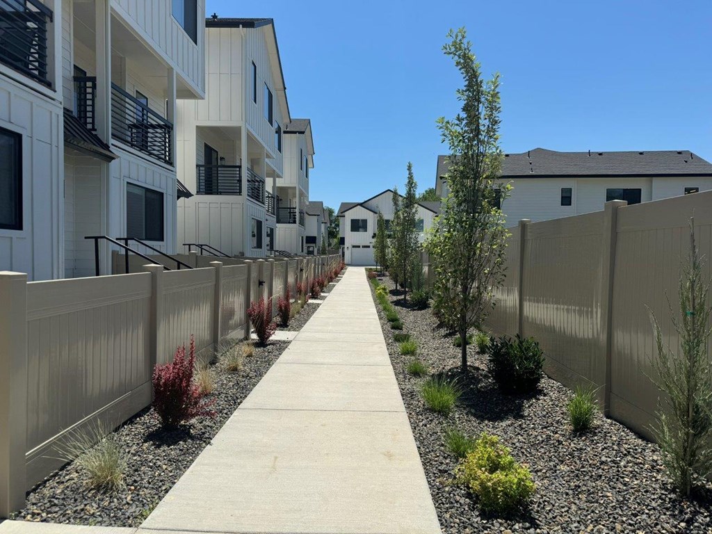 A long concrete walkway separates a row of white buildings.