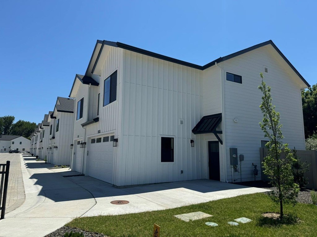 A white building with a black roof and a tree in front.