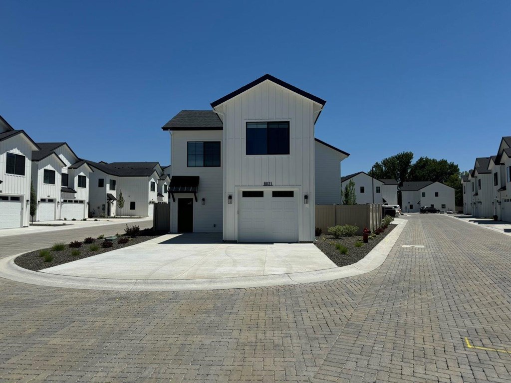 A white house with a black roof is surrounded by other similar houses.