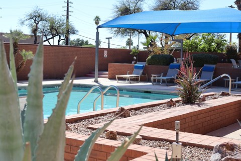 A pool surrounded by chairs and a blue umbrella.