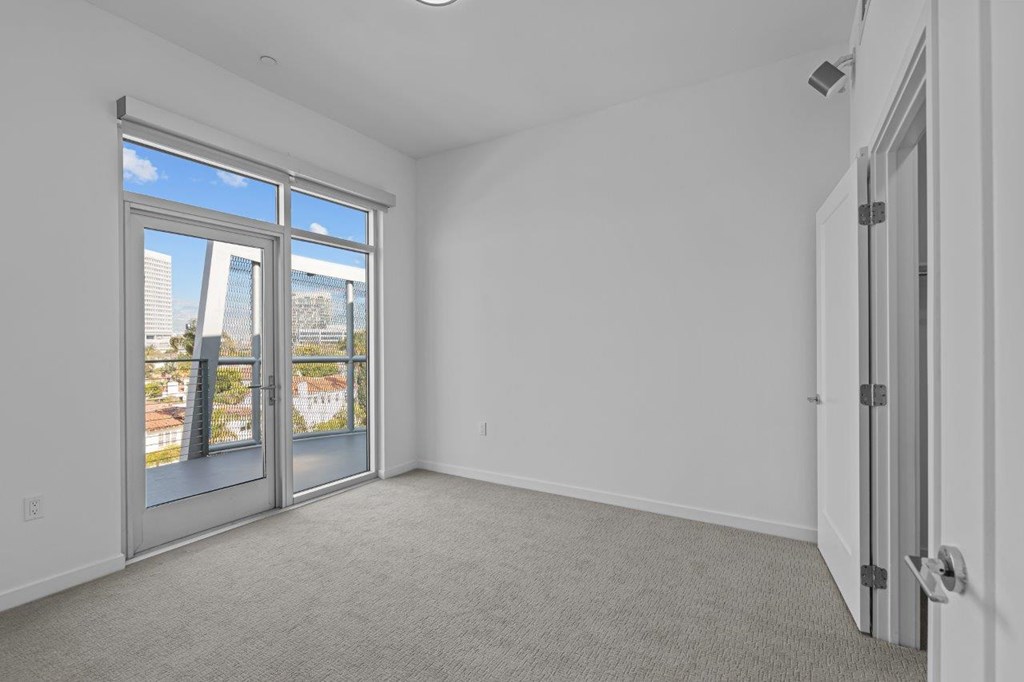 A room with a carpet floor, a white wall, and a sliding glass door.