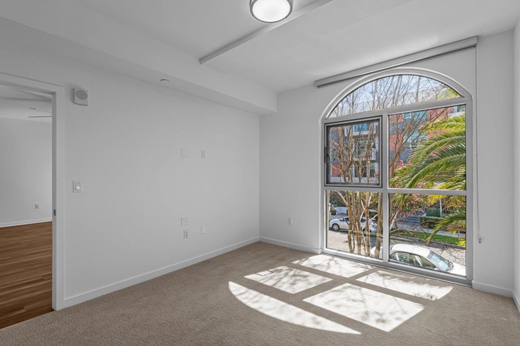 A room with a large window and a view of a street with cars and trees.