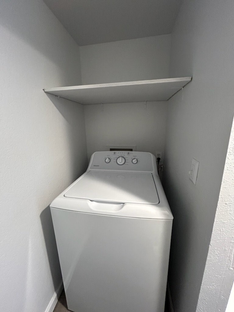 A white washing machine in a small, white-walled laundry room.
