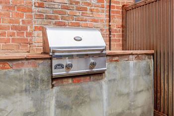 A BBQ grill is mounted on a brick wall.