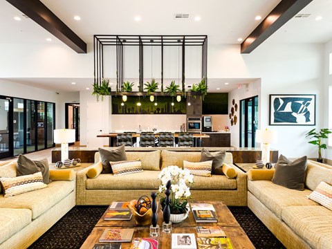 A modern living room with a large yellow sofa and a coffee table with magazines and a vase of flowers.