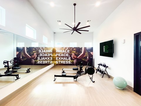 A gym room with exercise equipment and a wall mural promoting inhalation, exhalation, peace, and stress relief.