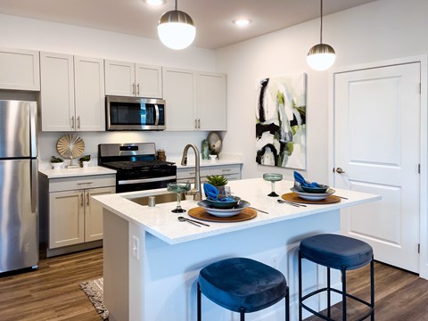 A modern kitchen with a white island and blue stools.