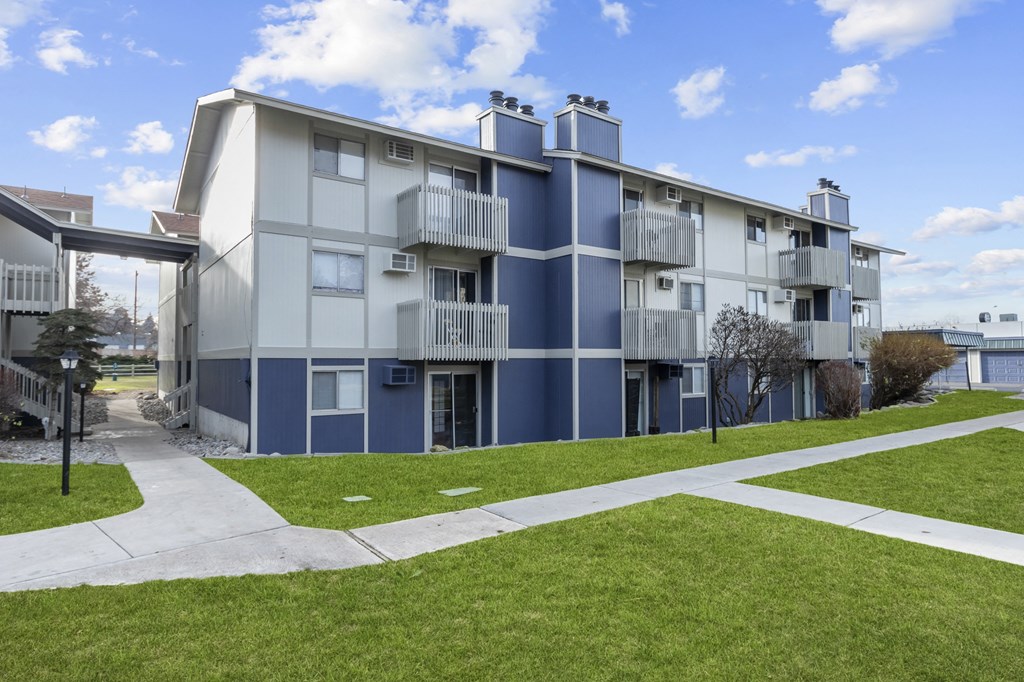 a blue and white apartment building with a sidewalk and grass