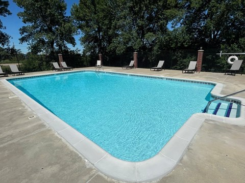 A swimming pool surrounded by trees and lounge chairs.