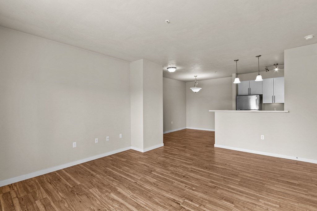 an empty living room with a kitchen in the background