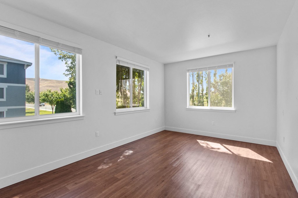 a bedroom with hardwood floors and three windows