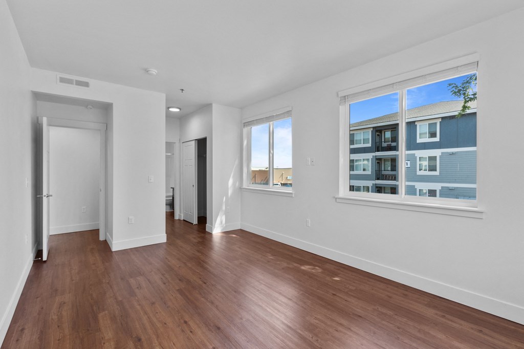 a bedroom with hardwood floors and three large windows