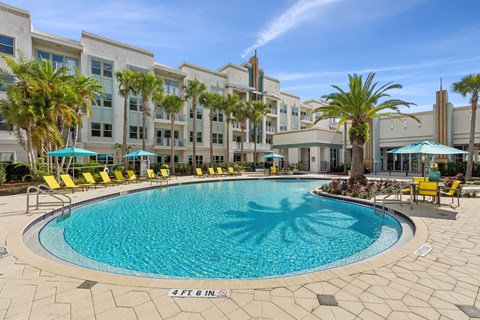 A large swimming pool surrounded by yellow chairs and palm trees.