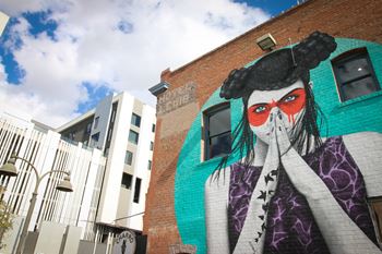 A mural of a woman with red eyes and black hair is painted on a brick wall.