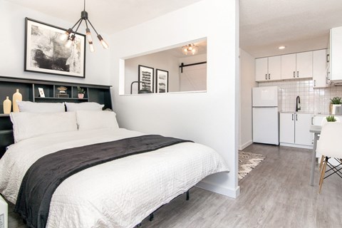 a bedroom with a bed and a kitchen in the background