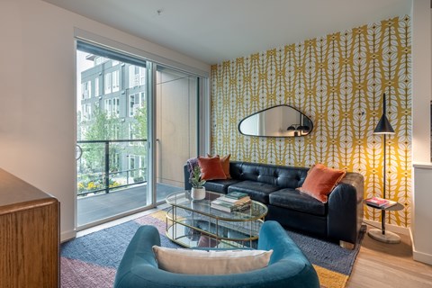A living room with a black couch and a yellow patterned wallpaper.