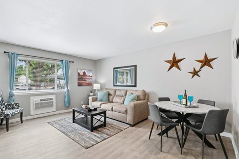 A living room with a white table and chairs, a couch, and a window with blue curtains.