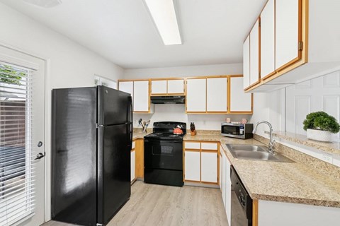 A black refrigerator stands in a kitchen with wooden cabinets and a sink.