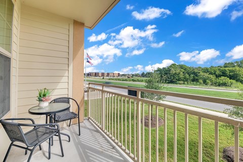 A balcony with a table and chairs overlooking a green landscape.