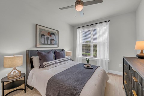 A bedroom with a large bed, a ceiling fan, and a painting on the wall.