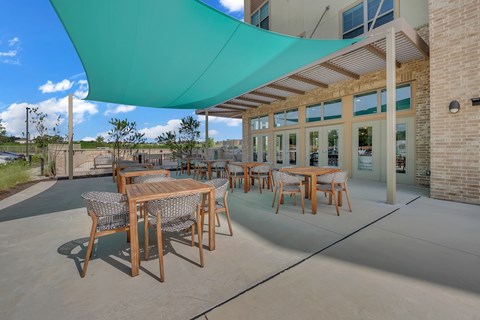 A patio with tables and chairs under a blue shade sail.