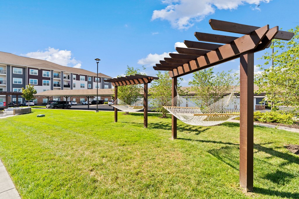 A wooden pergola with a hammock hangs over a grassy area.